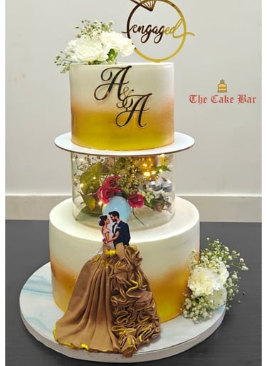 An elegant three-tier engagement cake featuring a gold ombré finish, custom initials, and a romantic