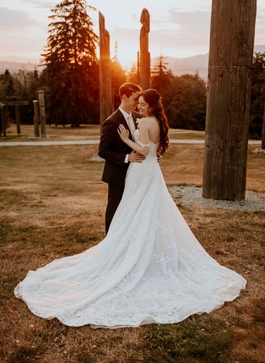 A bride in a lace wedding dress and groom embrace at sunset