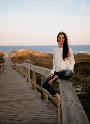 Michael Alexa Pitts smiling & sitting on the railing of a boardwalk path over the sand dunes & down to the beach near sunset
