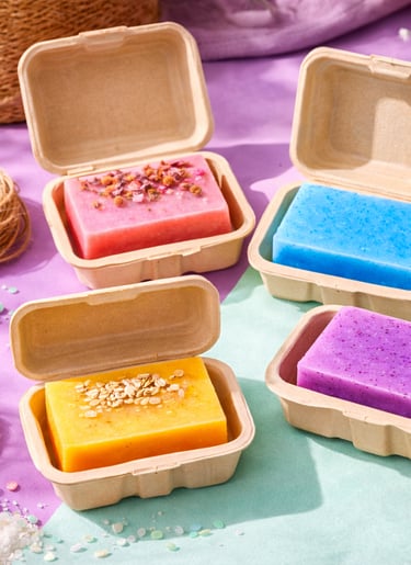 Eco-friendly clamshell packaging opened to reveal handmade soaps inside.