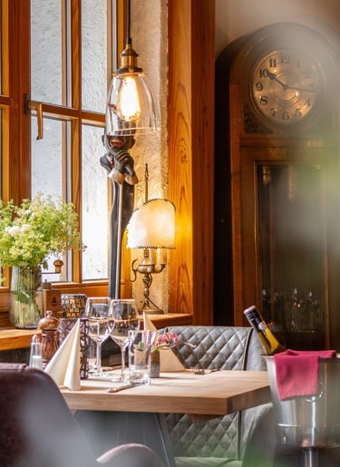 Eleganter Restauranttisch mit Weingläsern, antiker Standuhr und warmer Ambientebeleuchtung