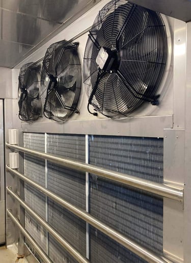 Industrial evaporator unit with three large fans and cooling coils inside a commercial walk-in freezer.