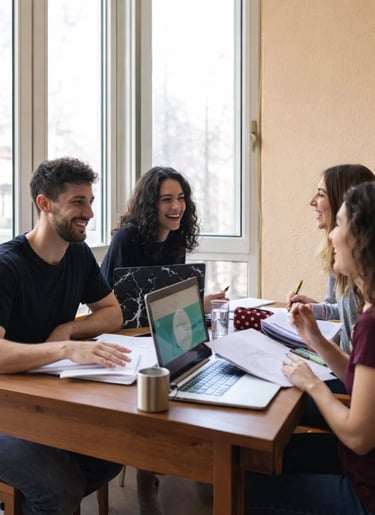 Diverse group of smiling university students studying together with laptops and notebooks at a table.