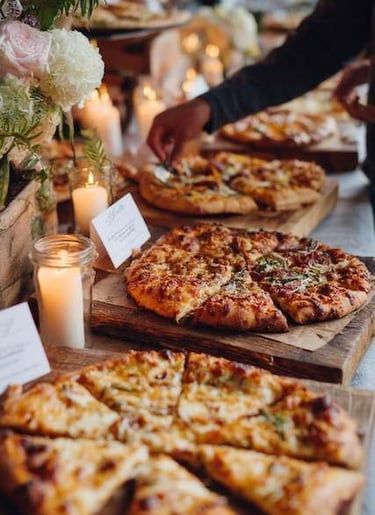 Exhibición de catering de pizza gourmet rústica, con velas y arreglos florales.