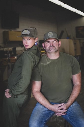 Alfred and Kandace, co-owners of Green Bee Laser, posing back-to-back in their restoration shop