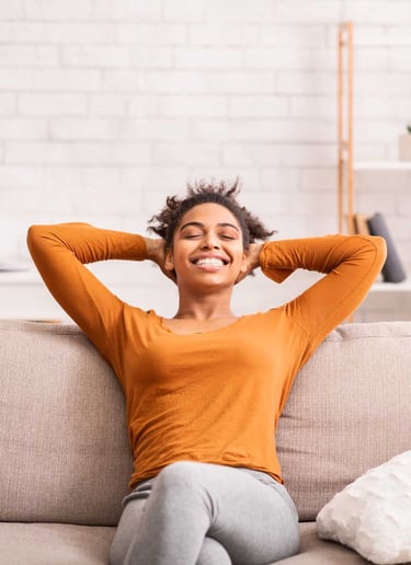 Smiling woman relaxing on a couch with her arms behind her head, enjoying a clean and tidy home envi