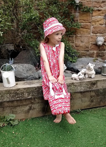 Young girl wearing a handmade a red dress with matching hat and bag made in Nottingham UK from sustainably sourced fabric