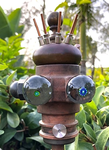 Found object robot head with glass eyes, one green pupil and a larger blue pupil.