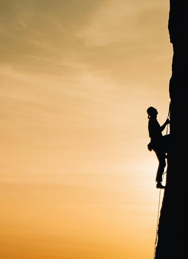 Silhouetted climber scaling steep rock face with ropes, symbolizing courage and adaptability.