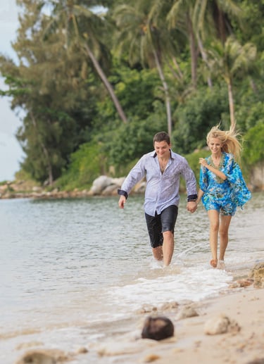 A happy couple holding hands and running along a tropical beach on Koh Samui, Thailand