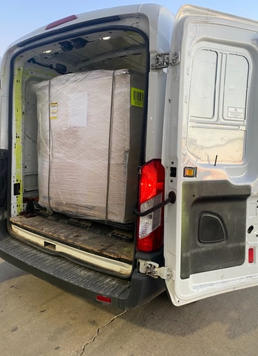 Rear view of a white delivery van with its rear doors open showing a large shrink-wrapped pallet