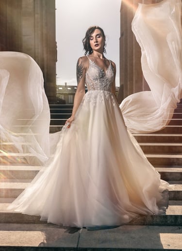 Woman in a flowing white gown standing on architectural steps, with fabric billowing in the wind.