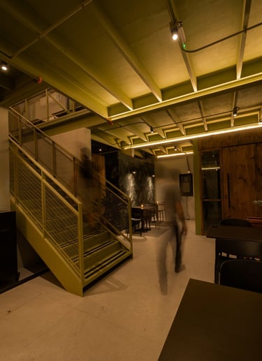 Un hombre caminando por un pasillo con una escalera, iluminacion indirecta.