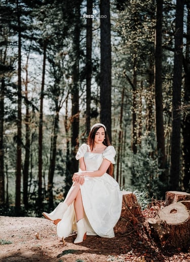 Bride sitting gracefully among tall forest trees in Surrey, photographed by Fred Art Studio.