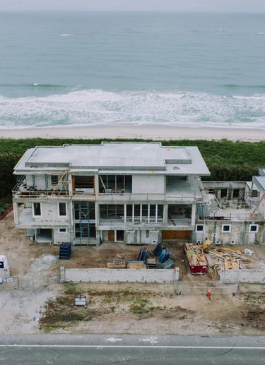 Aerial view of a luxury beachfront home under construction on a tropical coastline.