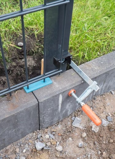 Fixation de clôture rigide sur muret en cours d’installation, avec pince de serrage et platine métal