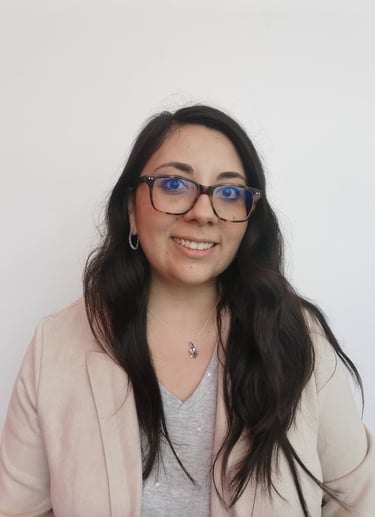 Smiling woman with long dark hair wearing glasses and a beige blazer against a white background.