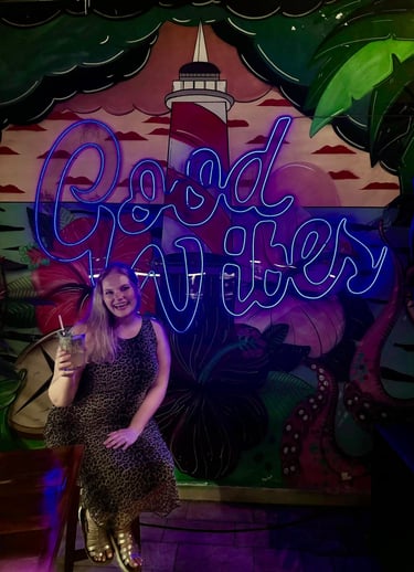 Woman holding a drink in front of neon sign saying "Good Vibes"