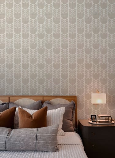 Cozy modern bedroom with beige tulip-patterned wallpaper, layered pillows, and a wooden headboard.