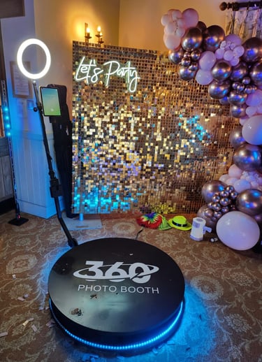 A 360 photo booth with ring light and gold shimmer wall backdrop for event party rentals.
