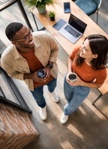Two people smiling in working environment, with hot drinks, seen from above