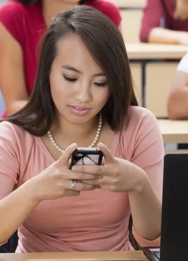 a woman sitting at a desk with a laptop and a cell phone