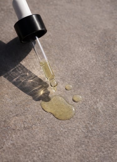 Glass dropper dispensing yellow facial oil serum onto a stone surface in natural sunlight.