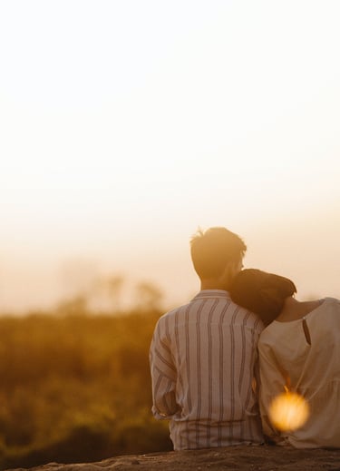 Couple de dos assis face à un paysage de soleil couchant.