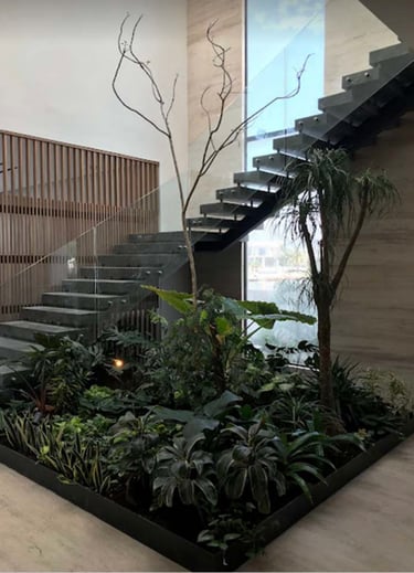 Modern interior design featuring a floating staircase over a lush indoor garden with tropical plants.