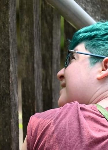 An image of the artist from behind, looking up and to the left. They have short teal hair.