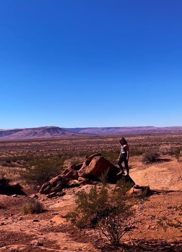 A hiker stands on a desert rock overlook with Arizona canyon mountains under a clear blue sky.