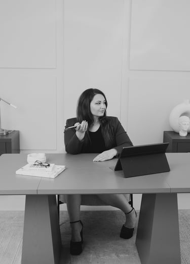 Adriana sitting at a desk with a tablet and phone in a modern office.