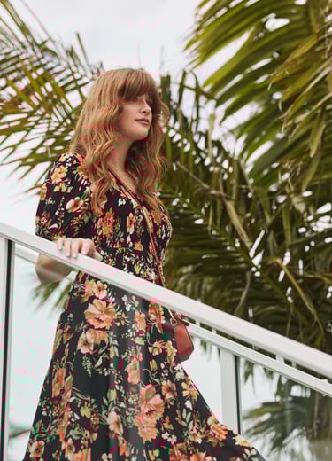 Fashion campaign photography - a woman in a floral dress standing on a balcony railing