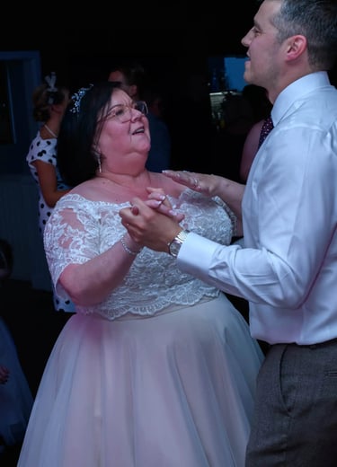 Smiling bride in lace wedding dress dancing with her son at a wedding reception.