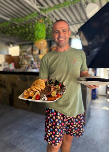 A smiling server holding a large platter of fresh Mediterranean grilled seafood and fried calamari.