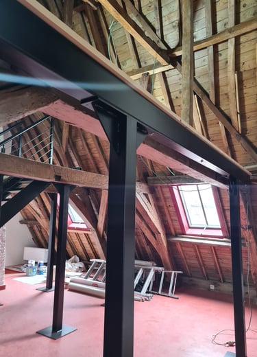 Structure métallique installée dans des combles avec charpente bois apparente – support pour mezzani