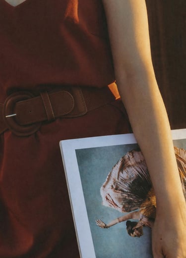 Une personne portant une robe couleur rouille avec une ceinture assortie, tenant un grand magazine