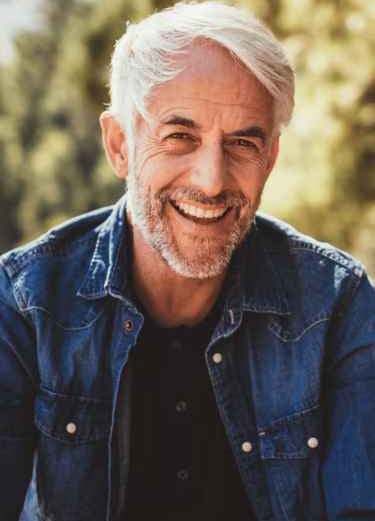 Ein Mann in jeans mit Bart, der lächelt.