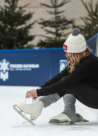 A woman in winter gear sitting on the ice and tying her white figure skates at the outdoor ice rink 