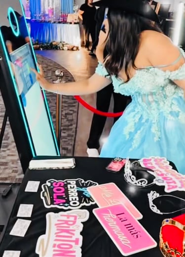 Girl in a blue dress at a Quinceañera interacting with a Mirror Photo Booth with props on the table.
