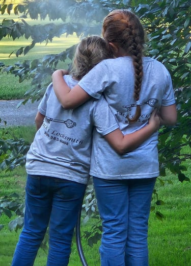 Two daughters hugging outdoors while wearing matching locksmith work shirts
