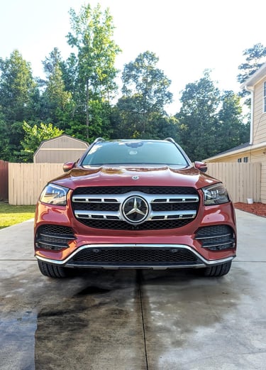 Front view of a red Mercedes-Benz GLS SUV parked on a concrete driveway in front of a house.