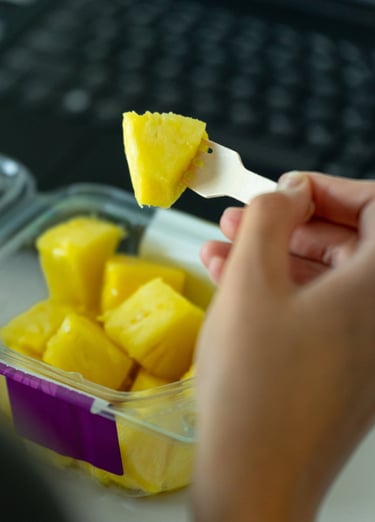 atidarytas pjaustytų ananasų indelis ir vienas gabaliukas yra pasmeigtas ant šakutės