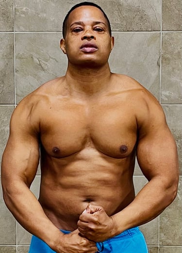Muscular man flexing chest and arm muscles in a bodybuilding pose against a tile wall.
