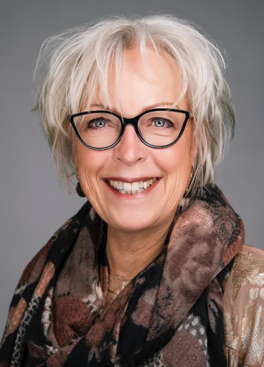 Professional headshot of a smiling senior woman with short white hair and stylish black glasses.