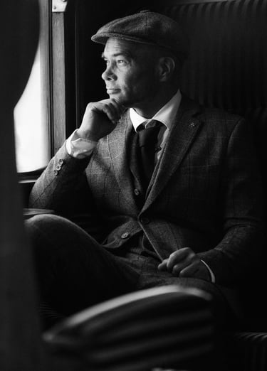 a man in a suit and hat sitting on a chair fashion shoot peaky blinders