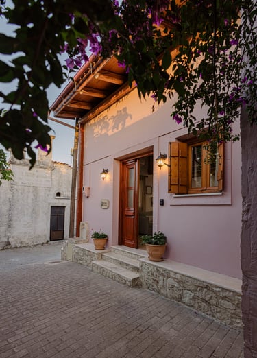 Charming cottage entrance: soft pink exterior, wooden doors, vibrant purple flowers
