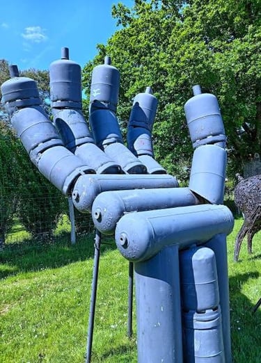 A large metal hand sculpture made of blue recycled gas cylinders standing in a green garden.