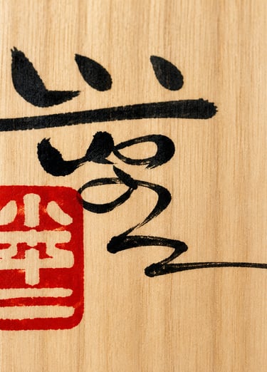 Traditional Japanese calligraphy and red hanko stamp on a light wood grain background.