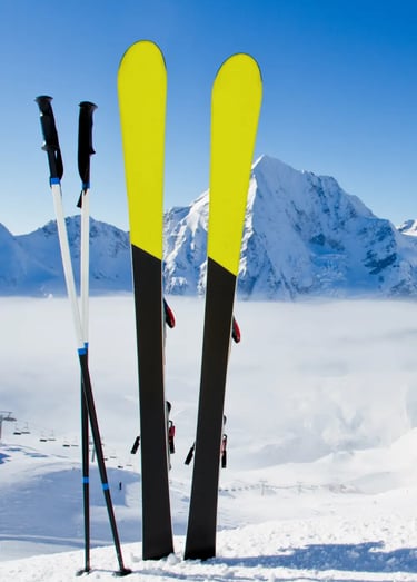 Pair of yellow skis and poles standing upright in fresh snow with mountains behind